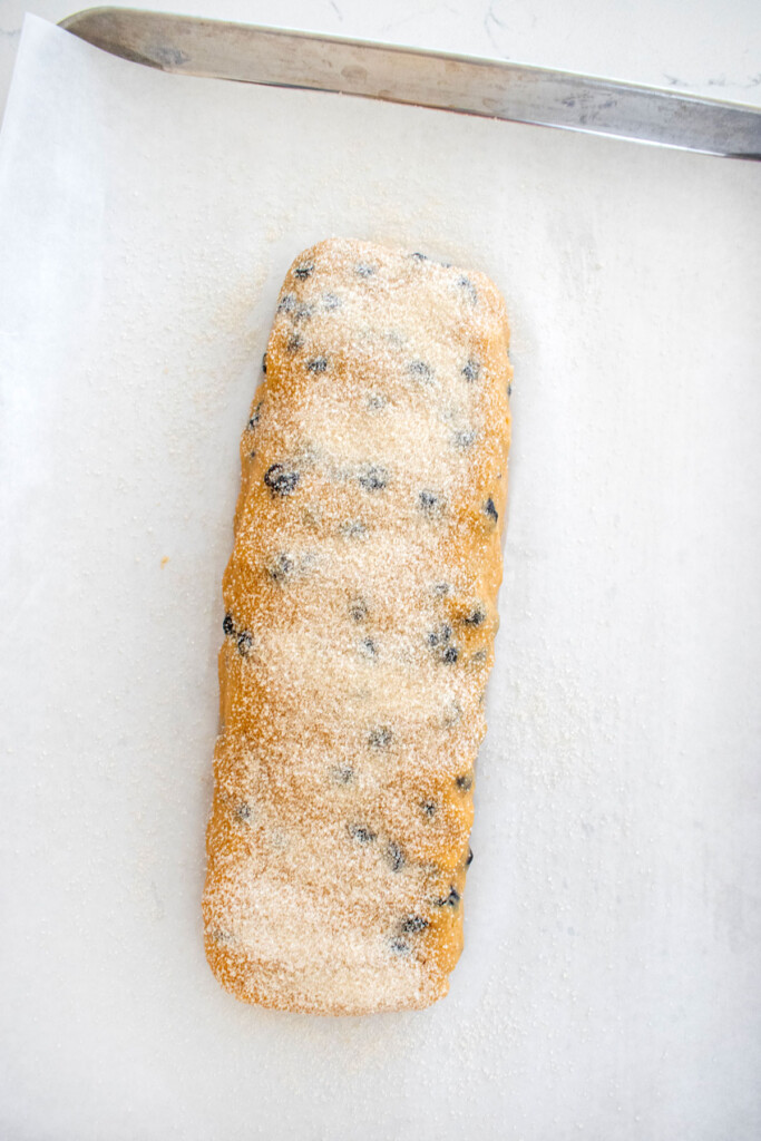 blueberry muffin biscotti cookie dough log on a baking sheet sprinkled with cane sugar.