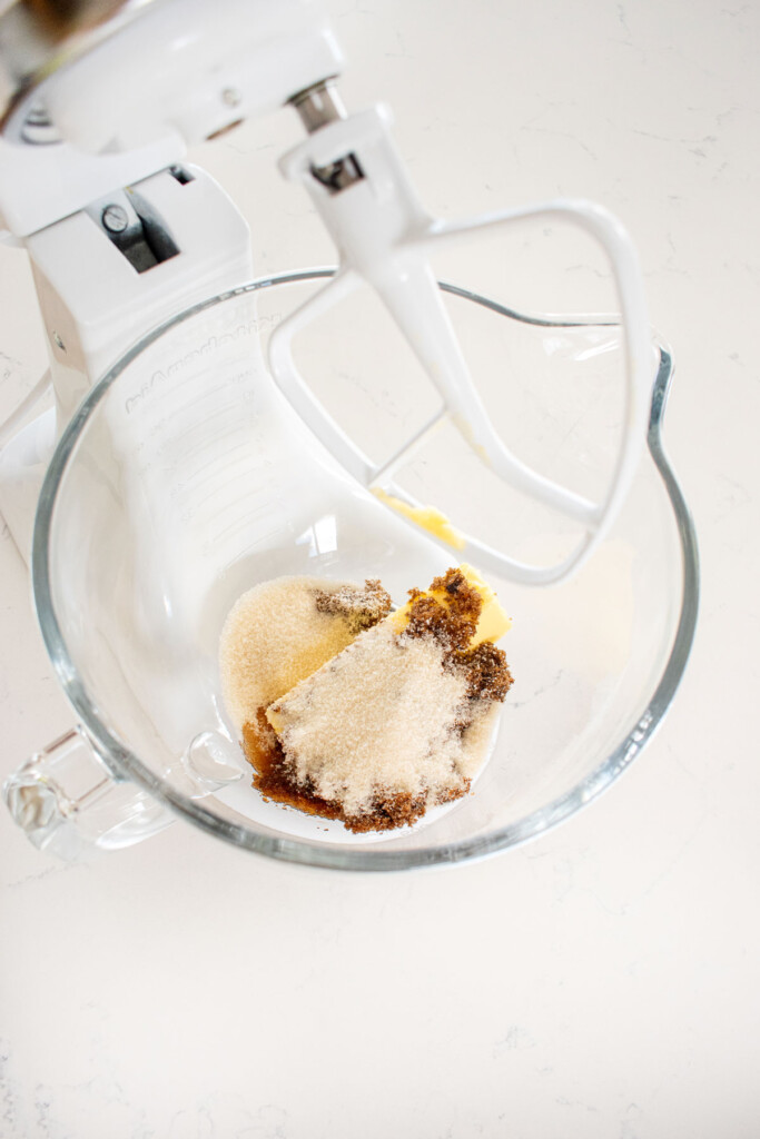 glass mixing bowl of butter and sugar on a white marble counter.