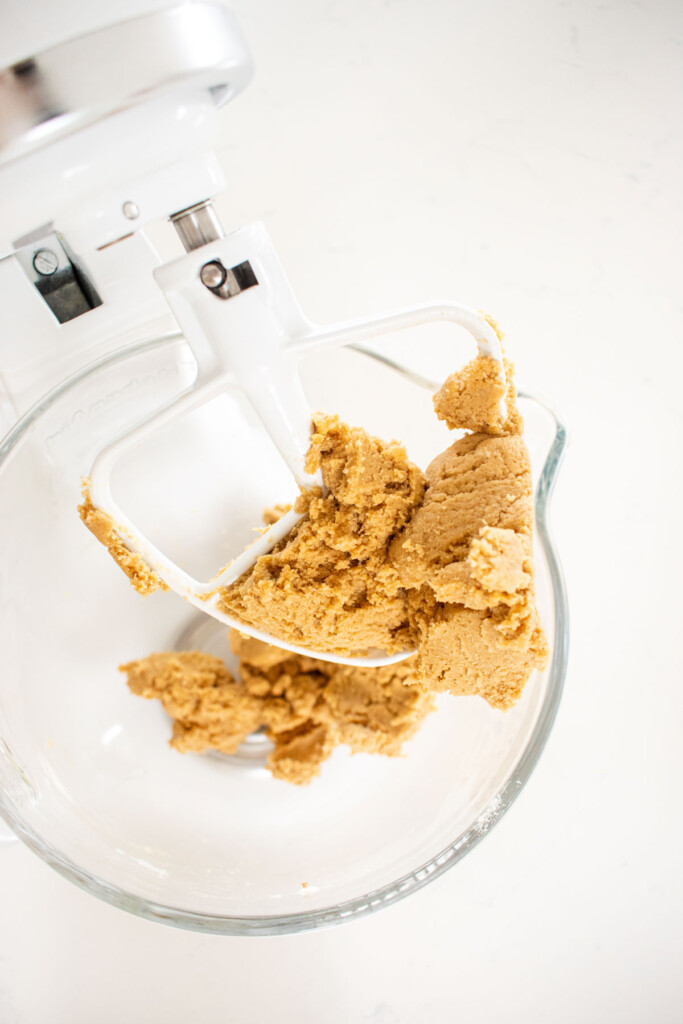 cream cheese chocolate chip cookie dough in a glass mixing bowl on a white marble counter.l