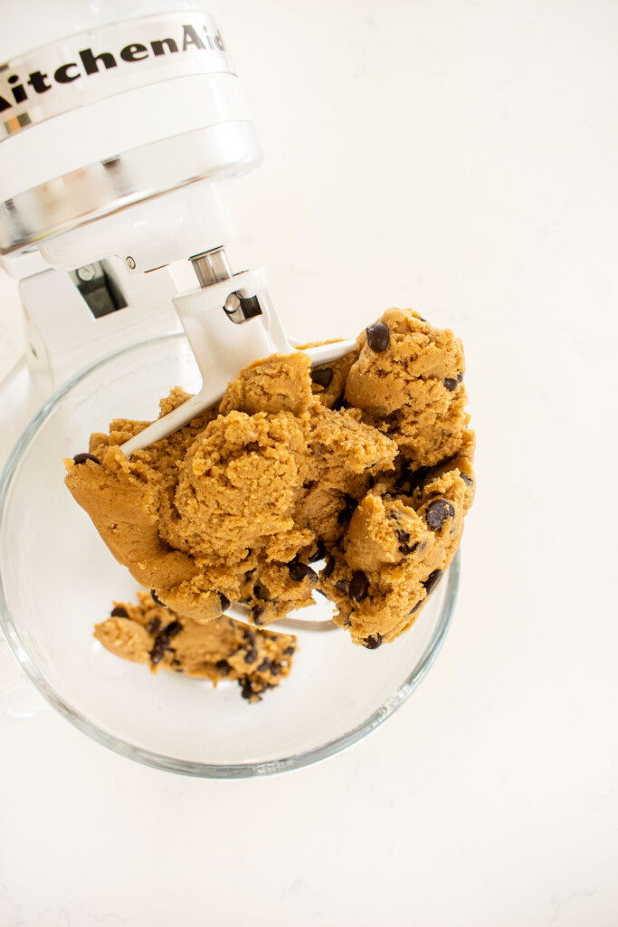 cream cheese chocolate chip cookie dough in a glass mixing bowl on a white marble counter.l