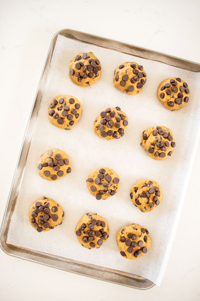 cream cheese chocolate chip cookie dough balls on a baking sheet on a white marble counter.