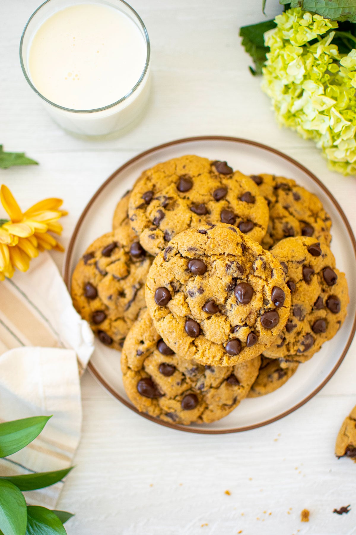 cream cheese chocolate chip cookies on a plate on a white wood counter with a glass of milk and fresh flowers.