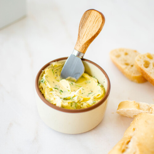 easy garlic herb butter in a small bowl with a wooden handled tiny knife and fresh bread on a marble table.
