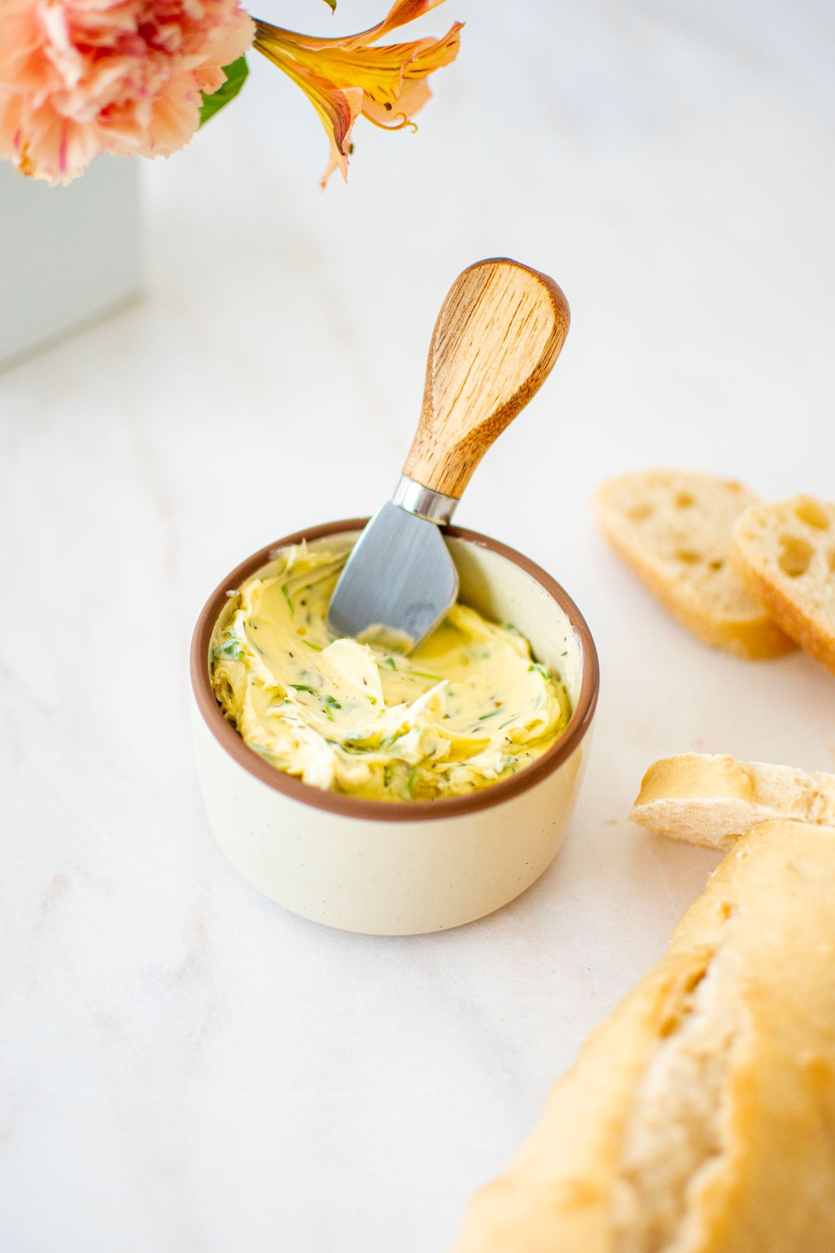 easy garlic herb butter in a small bowl with a wooden handled tiny knife and fresh bread on a marble table.