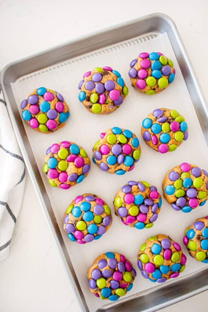 M&M cookie dough rolled in candies on a baking sheet on a marble counter.