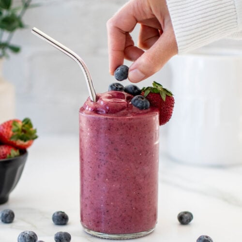 berry smoothie with woman adding a bluebery on top