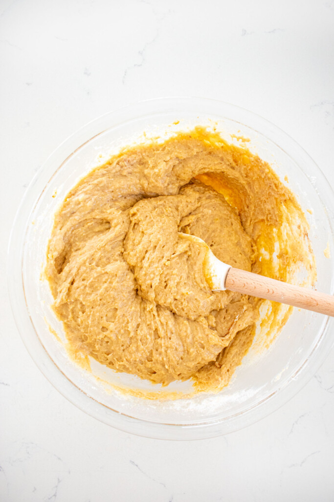 snickerdoodle baked donuts batter in a glass mixing bowl on a white marble countertop.
