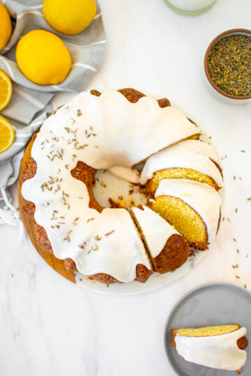 sourdough lavender lemon bundt cake cut into slices on a white marble serving board on a marble table.