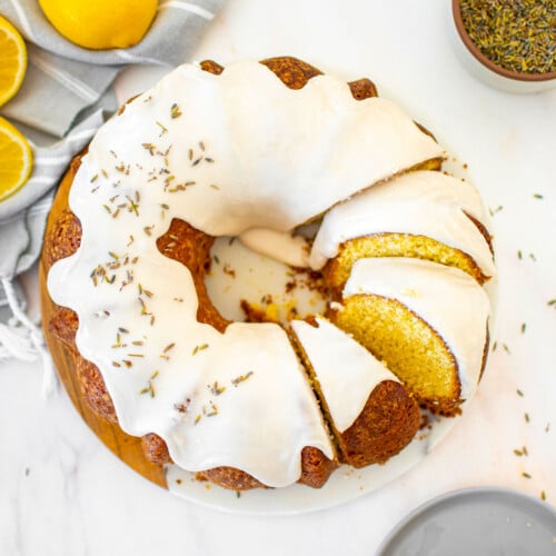 sourdough lavender lemon bundt cake cut into slices on a white marble serving board on a marble table.