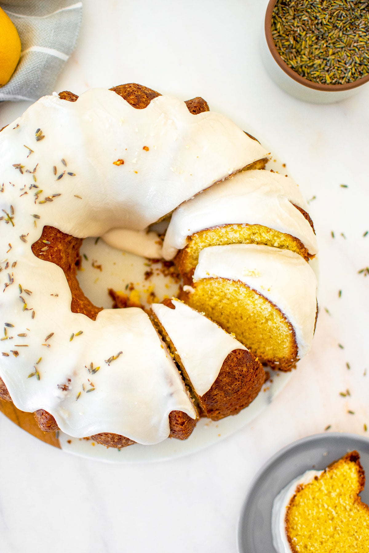 sourdough lavender lemon bundt cake cut into slices on a white marble serving board on a marble table.