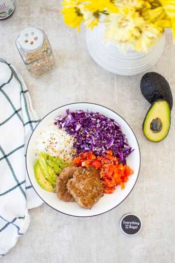 turkey avocado brunch bowl on a dining table with yellow flowers and avocado and everything bagel spice on the side.