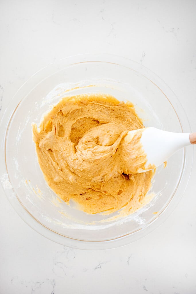 blueberry peanut butter dog cake batter in a glass mixing bowl with a spatula on a white marble countertop.