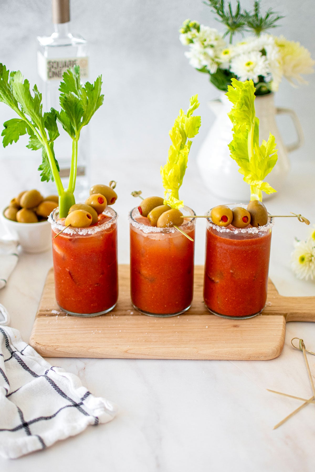 bone broth bloody marys with green olives and celery on a white marble counter.