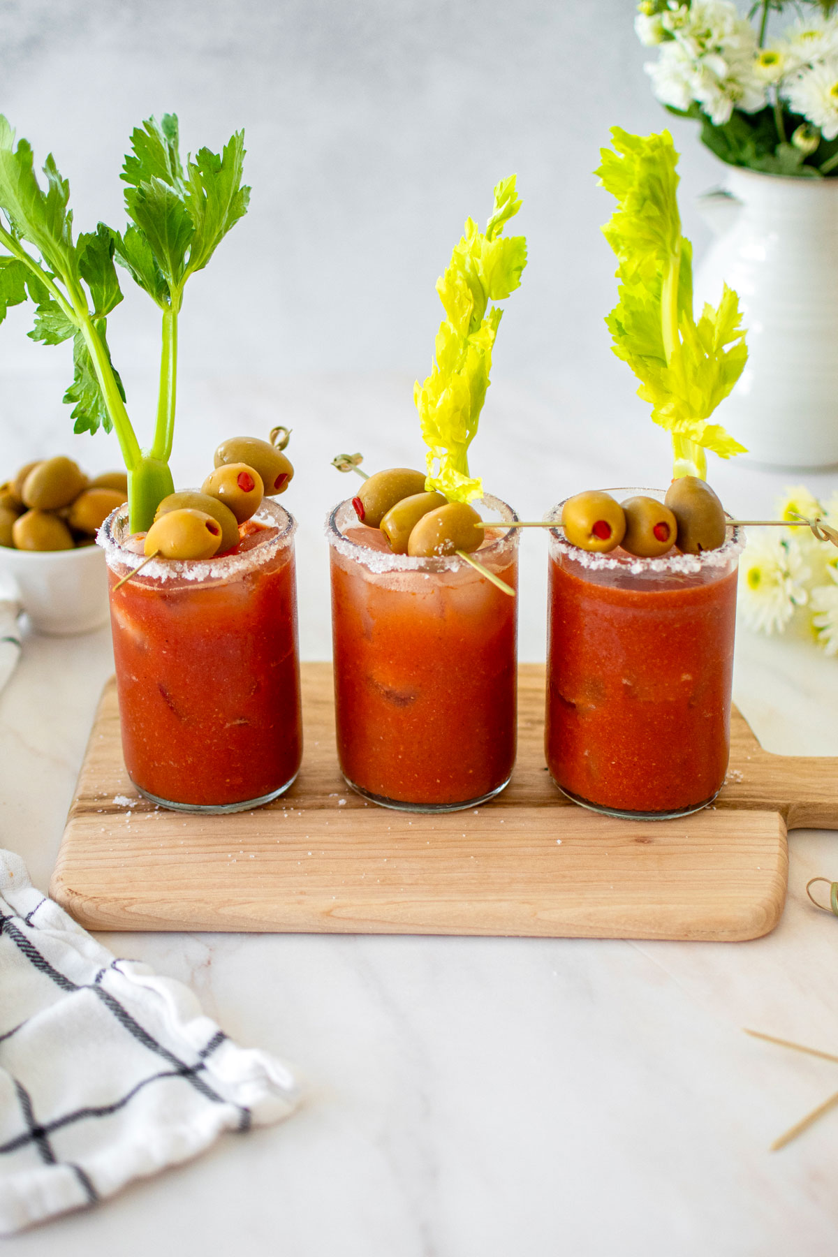 bone broth bloody marys with green olives and celery on a white marble counter.