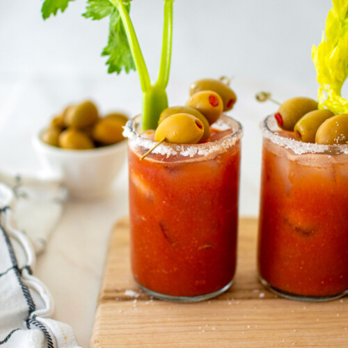 bone broth bloody marys with green olives and celery on a white marble counter.