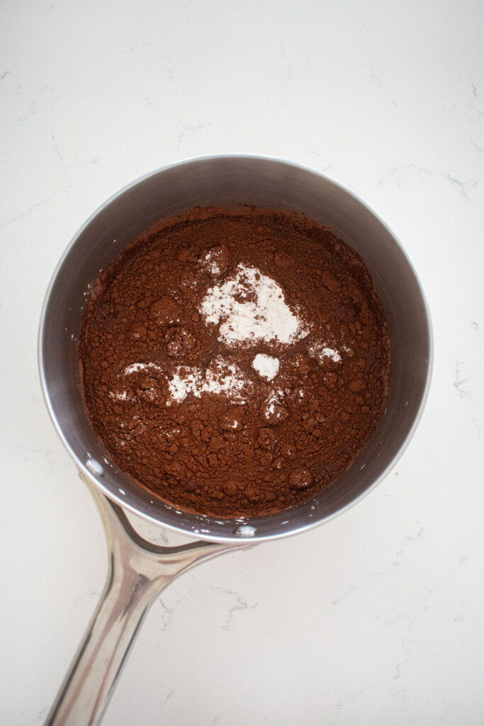 ingredients for eggless chocolate peanut butter pudding in a stainless steel pot on a marble counter.