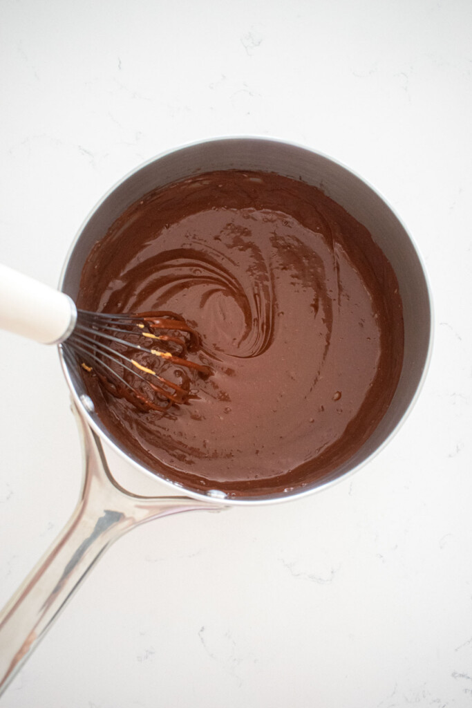 eggless chocolate peanut butter pudding being whisked together in a stainless steel pot on a marble counter.