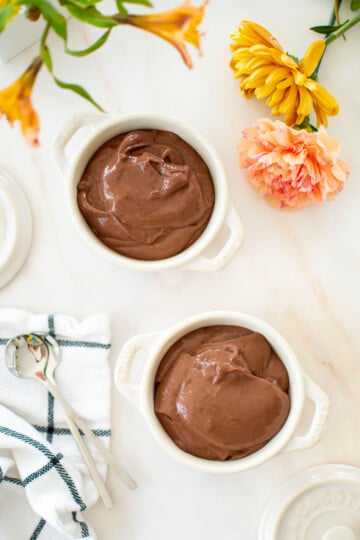 eggless chocolate peanut butter pudding in mini dutch ovens on a white marble counter with fresh flowers.