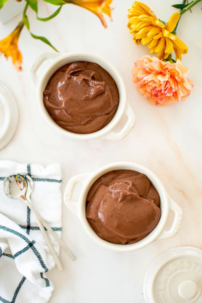 eggless chocolate peanut butter pudding in small ramekins on a marble counter with fresh flowers.