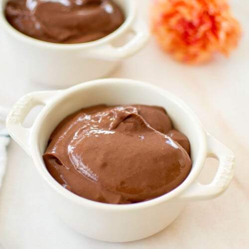 eggless chocolate peanut butter pudding in mini dutch ovens on a white marble counter with fresh flowers.