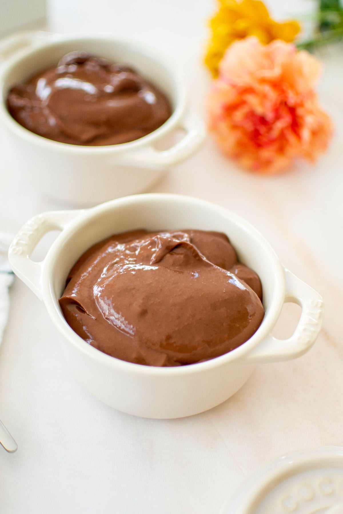 eggless chocolate peanut butter pudding in mini dutch ovens on a white marble counter with fresh flowers.