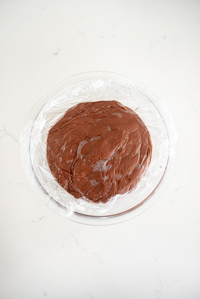 eggless chocolate peanut butter pudding in a glass bowl with plastic warp pressed on top of it.