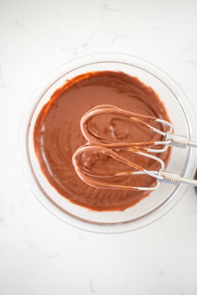 eggless chocolate peanut butter pudding being whipped with a hand mixer in a glass bowl on a marble counter.