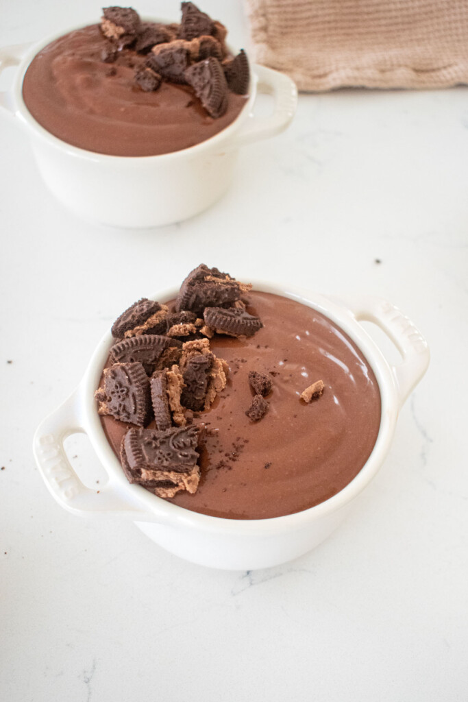 eggless chocolate peanut butter pudding in small ramekins with crush chocolate cookies on top on a marble counter.