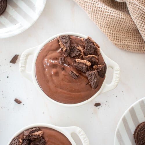 eggless chocolate peanut butter pudding in small ramekins with crush chocolate cookies on top on a marble counter.