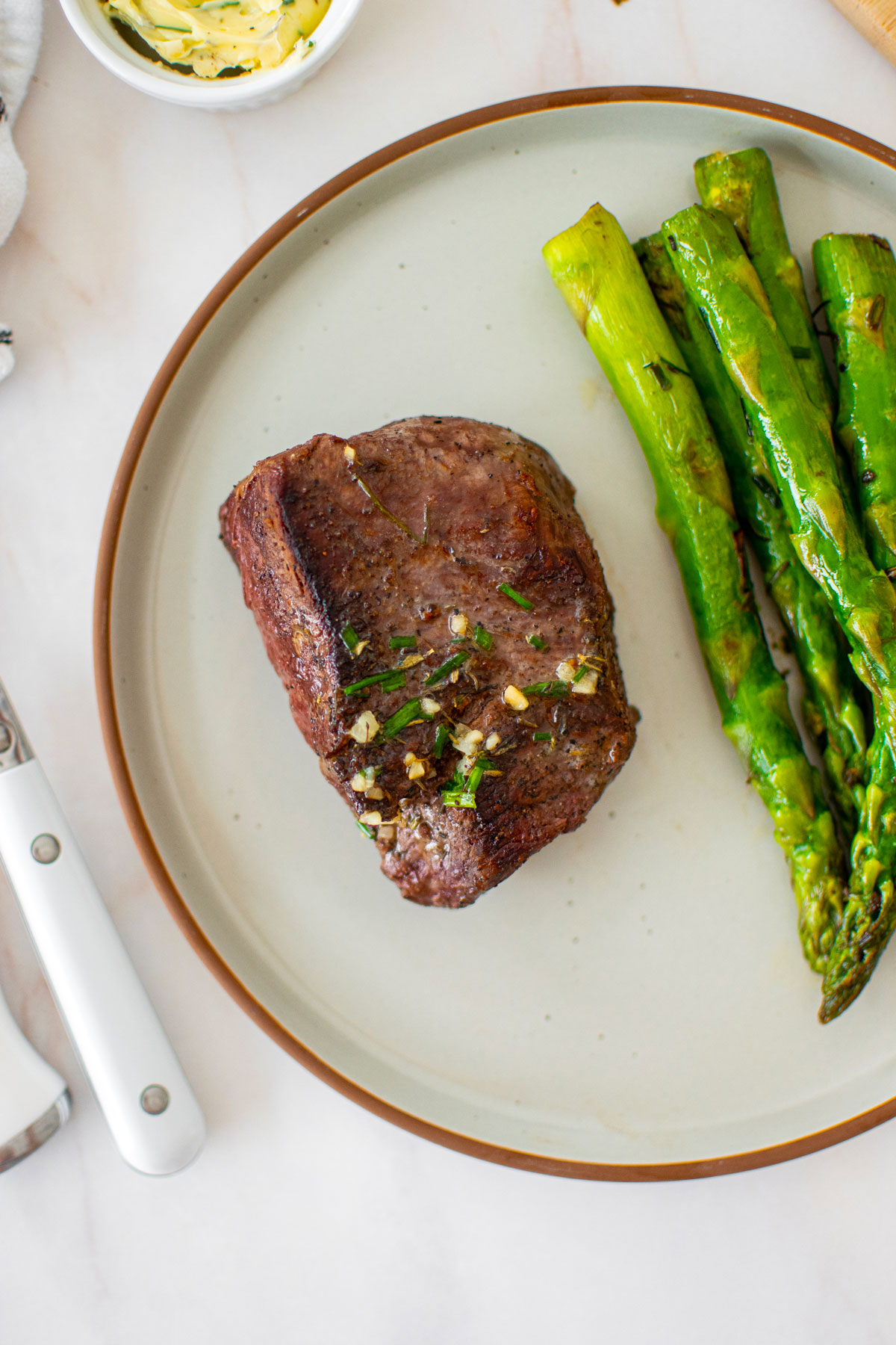 garlic herb beef tenderloin steak with garlic herb butter on a plate with asparagus.