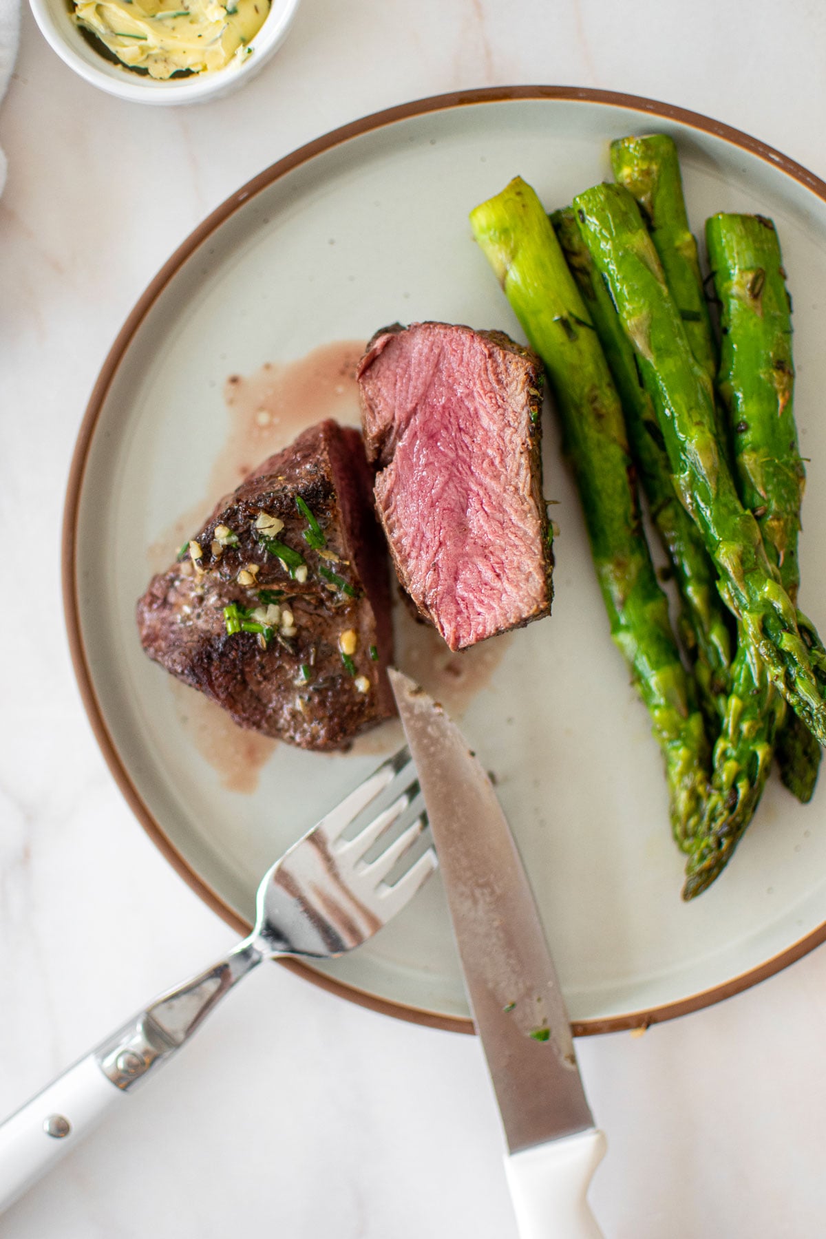 medium rare garlic herb beef tenderloin sliced in half on a plate with asparagus on a marble countertop.