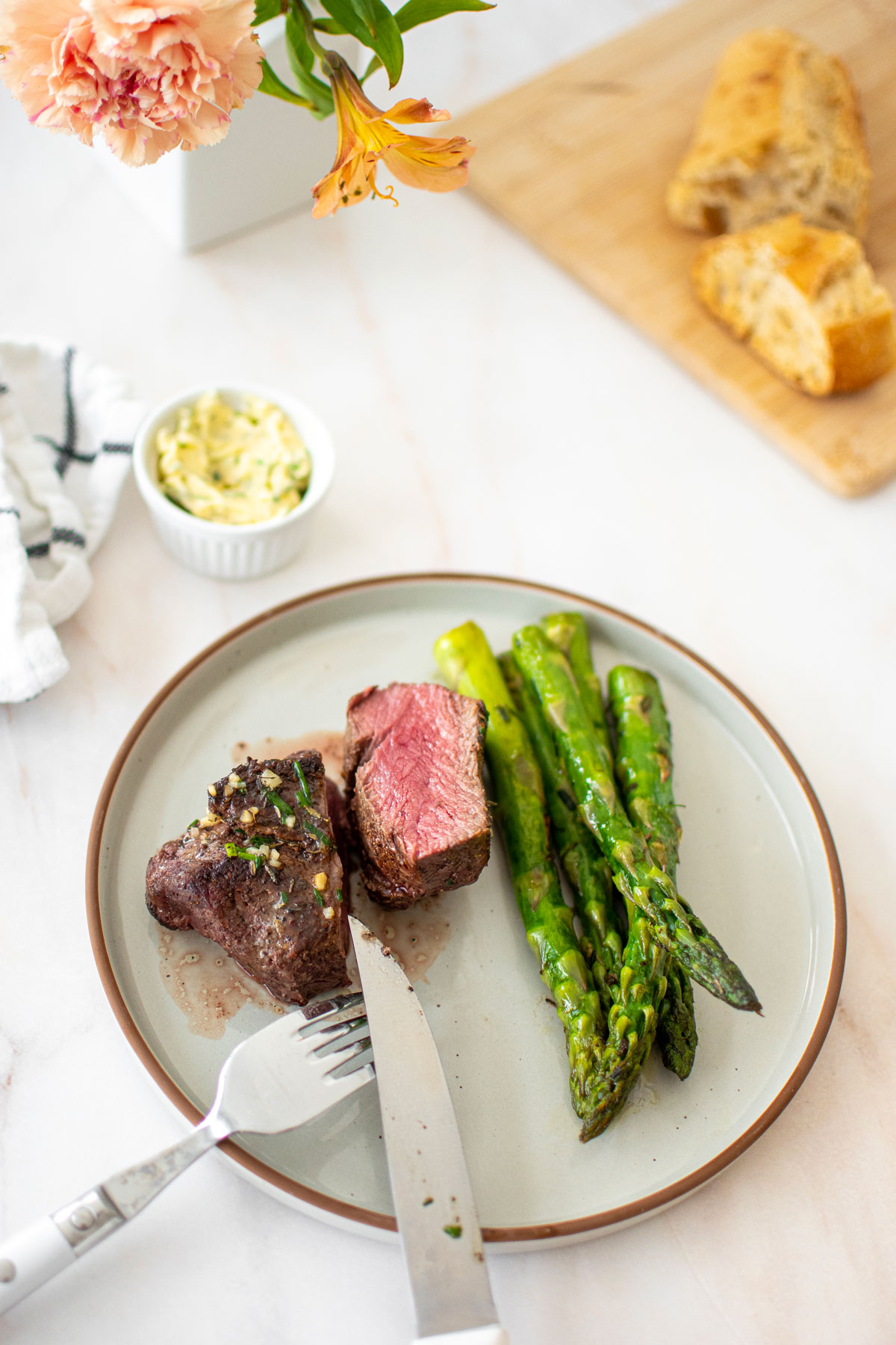 medium rare garlic herb beef tenderloin sliced in half on a plate with asparagus on a marble countertop.