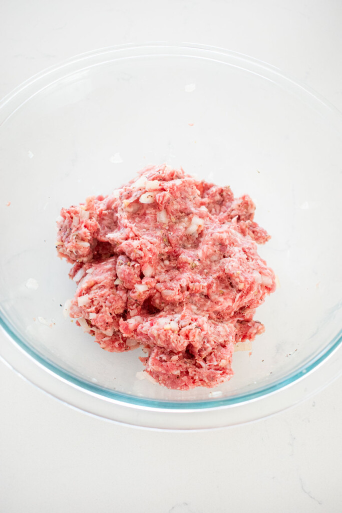 glass mixing bowl with ground beef and lamb and spiced all mixed together on a marble counter.