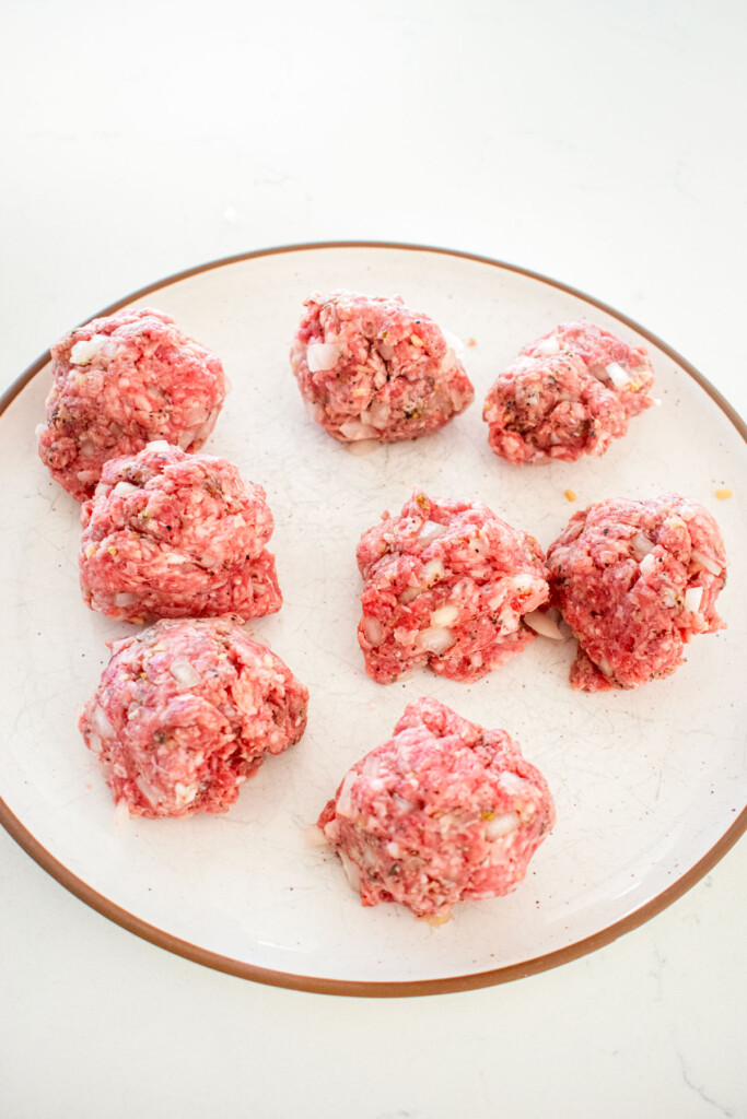 raw ground beef and lamb mixture formed into 8 even portions on a plate on a marble counter.