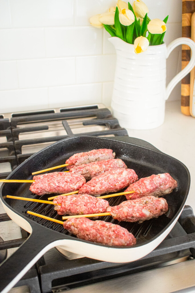 beef and lamb kabobs in a grill pan being seared on the stovetop.