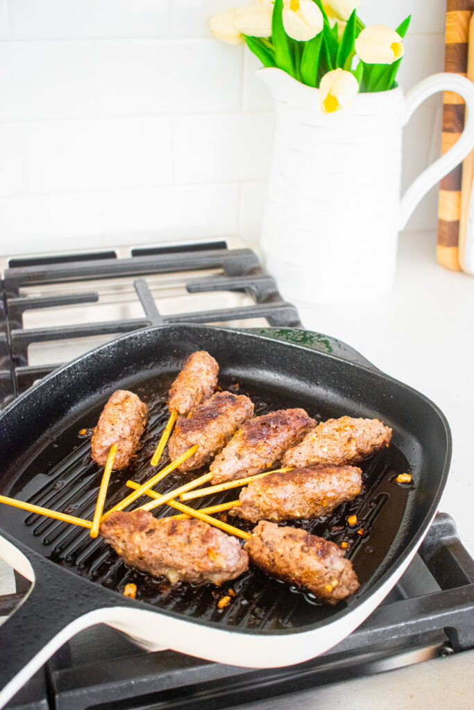 beef and lamb kabobs cooking on grill pan on a stovetop.