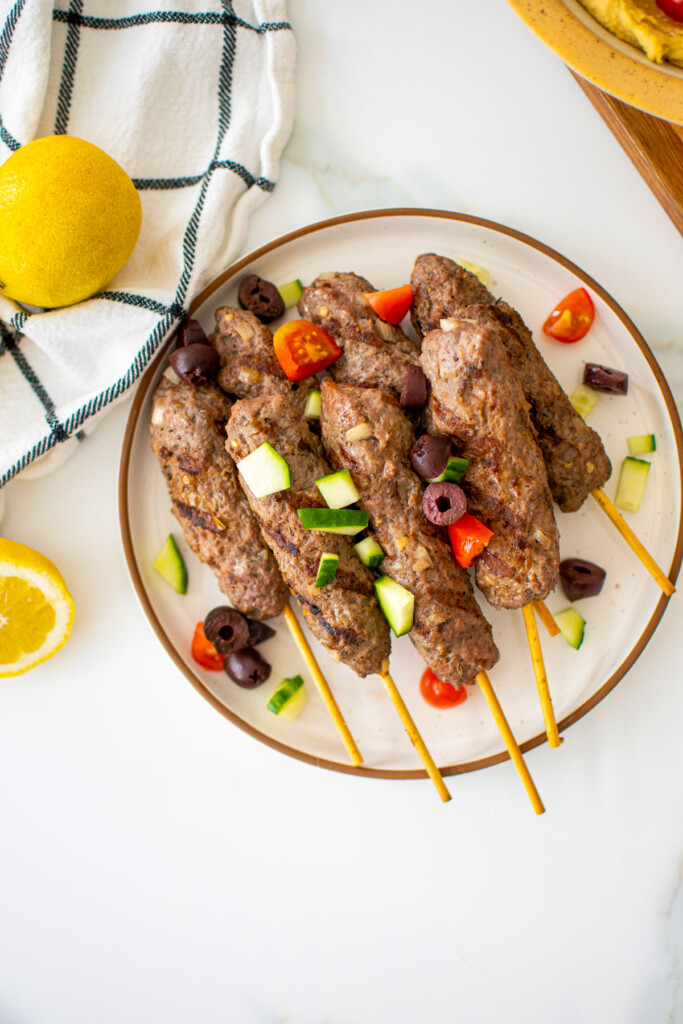 greek beef and lamb kafta kabobs on a plate on a marble countertop.