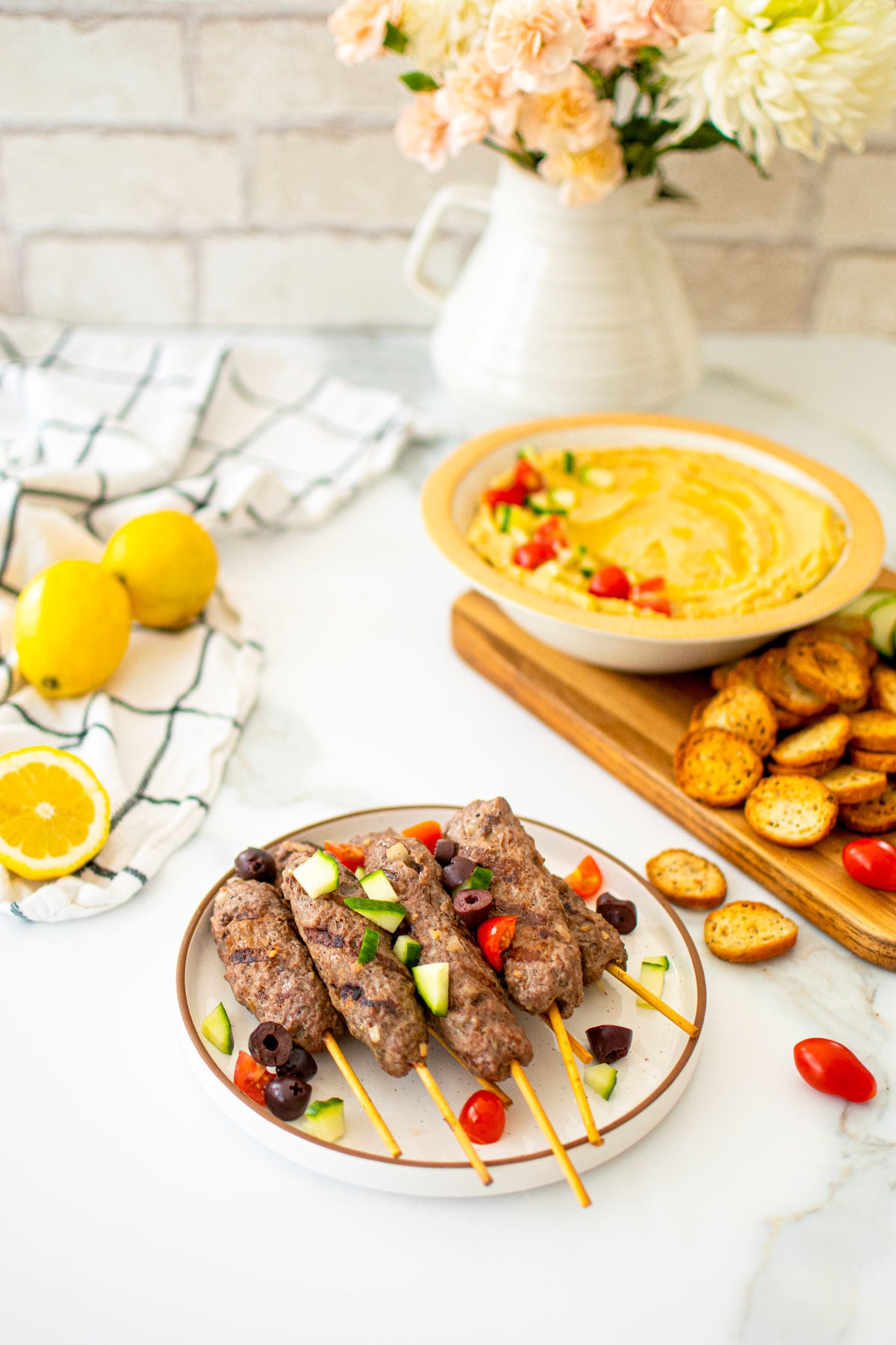 greek beef and lamb kafta kabobs on a plate on a marble table with lemon hummus.