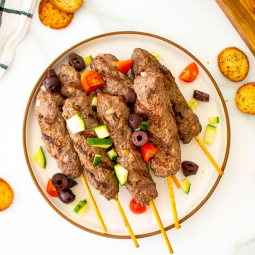 greek beef and lamb kafta kabobs on a plate on a marble countertop.