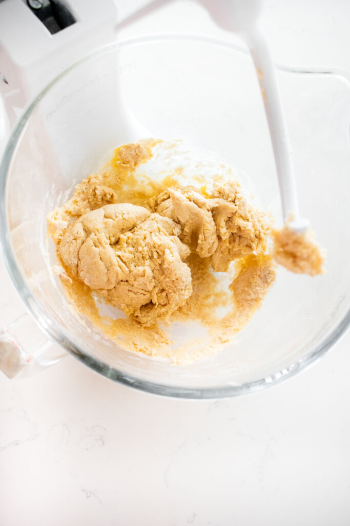 mixed sourdough hot dog bun dough in a glass stand mixing bowl on a white marble counter.