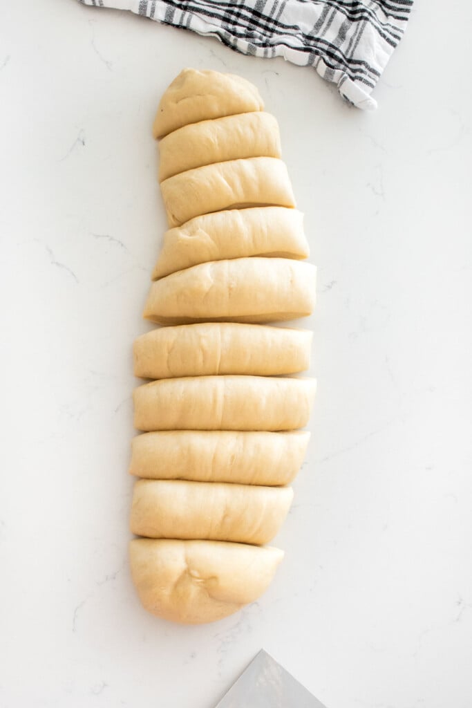 homemade sourdough hot dog bun dough divided into 10 pieces on a white marble counter.