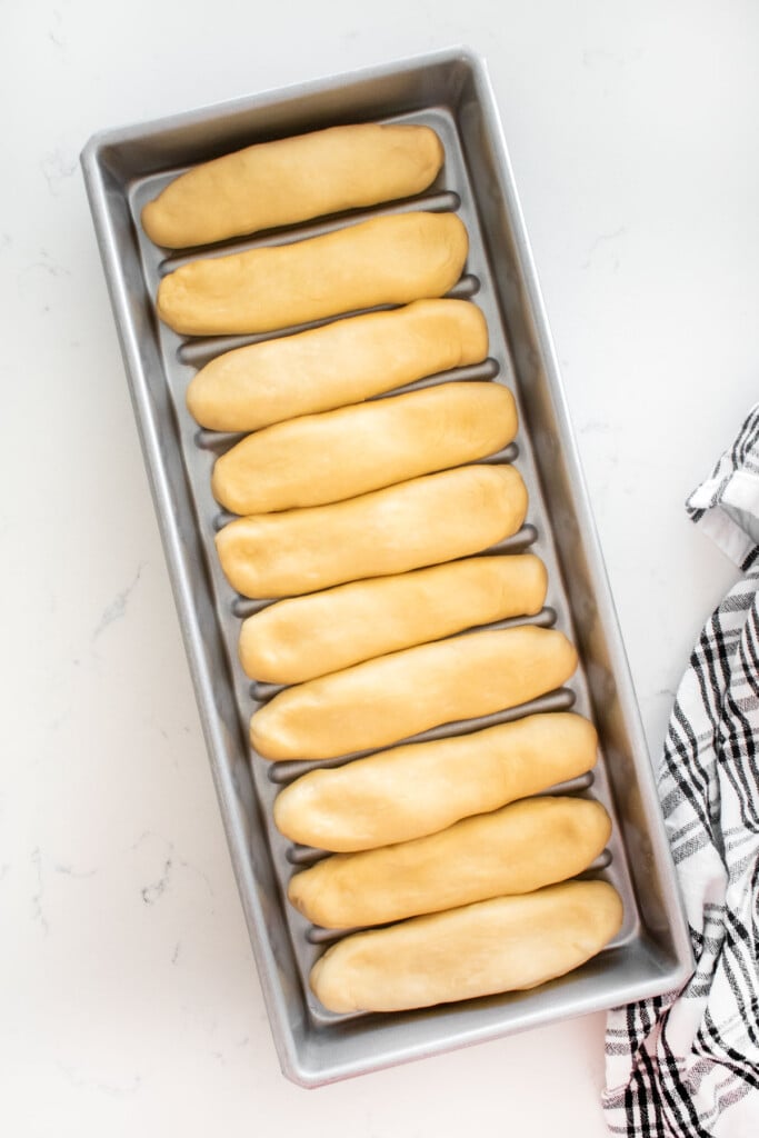 homemade sourdough hot dog bun dough in a hot dog pan on a white marble counter.