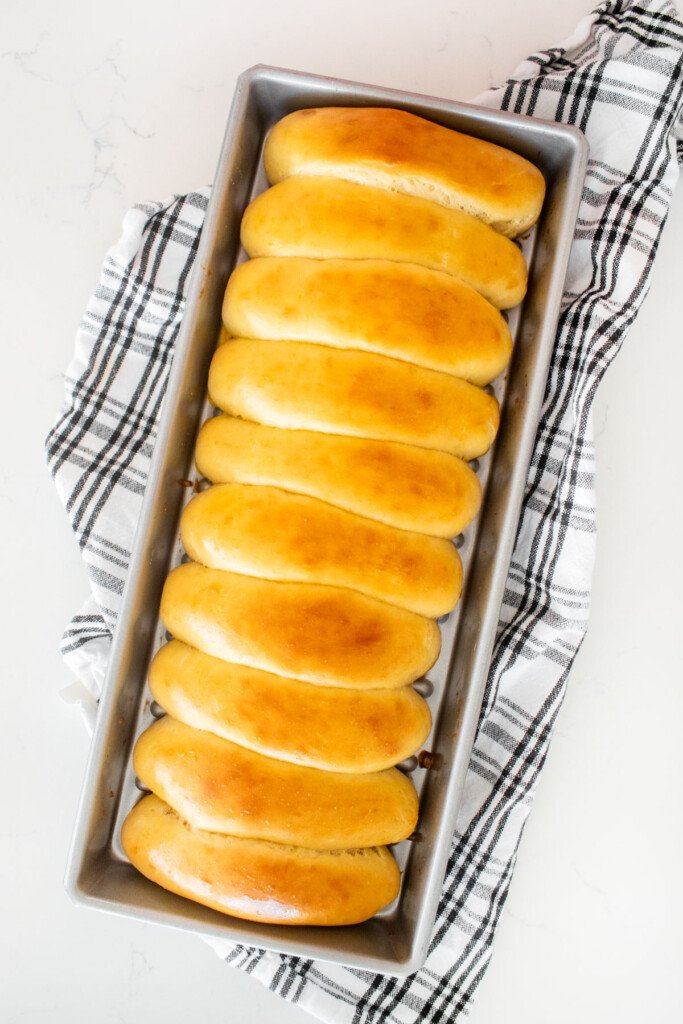 baked homemade sourdough hot dog buns in a hot dog pan on a white marble counter.