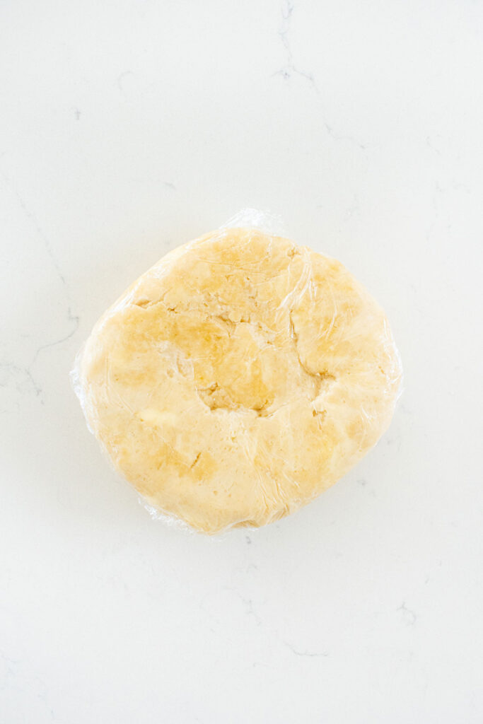 pie dough wrapped in plastic wrap on a white marble counte.r