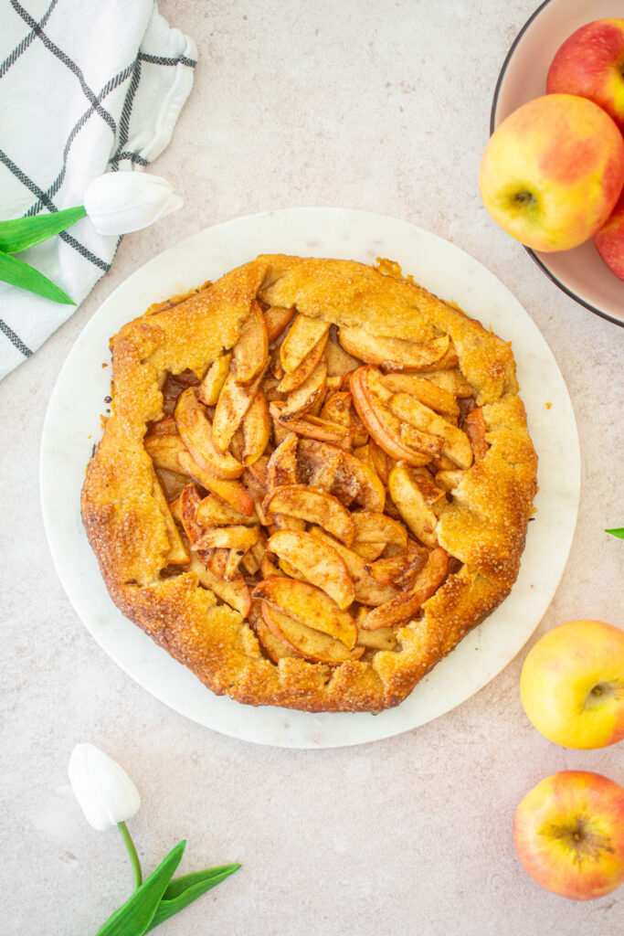 eggless honey apple galette on a round marble serving board with fresh apples and flowers.