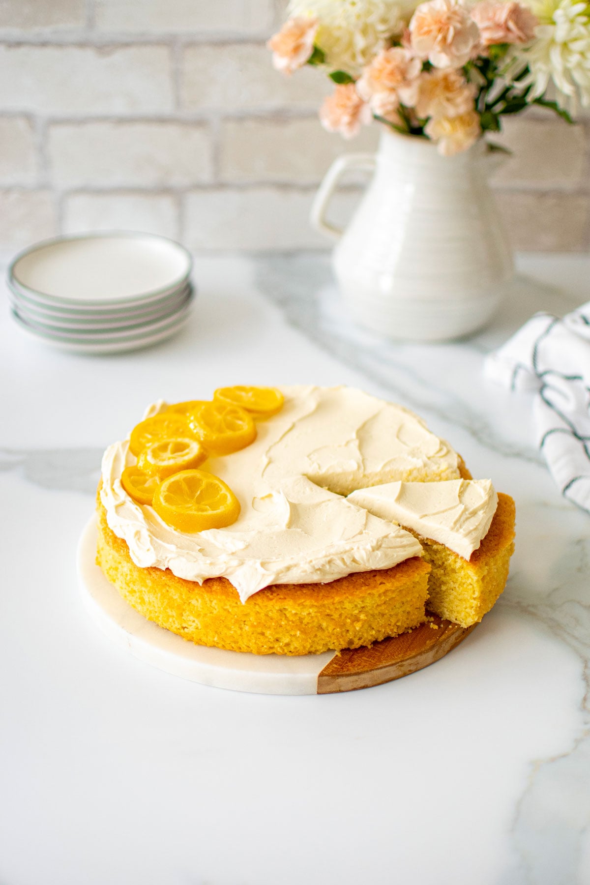 lemon olive oil snack cake on a marble counter with fresh flowers and cake plates.