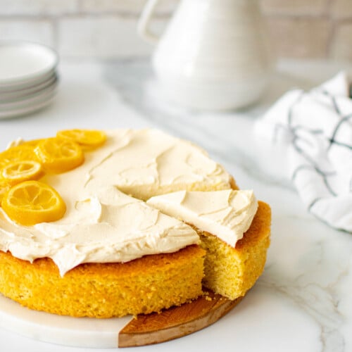lemon olive oil snack cake on a marble counter with fresh flowers and cake plates.