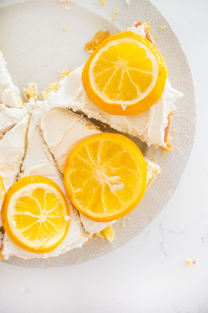 lemon olive oil snack cake with lemon frosting and candied lemons cut into slices on a plate on a white marble counter.