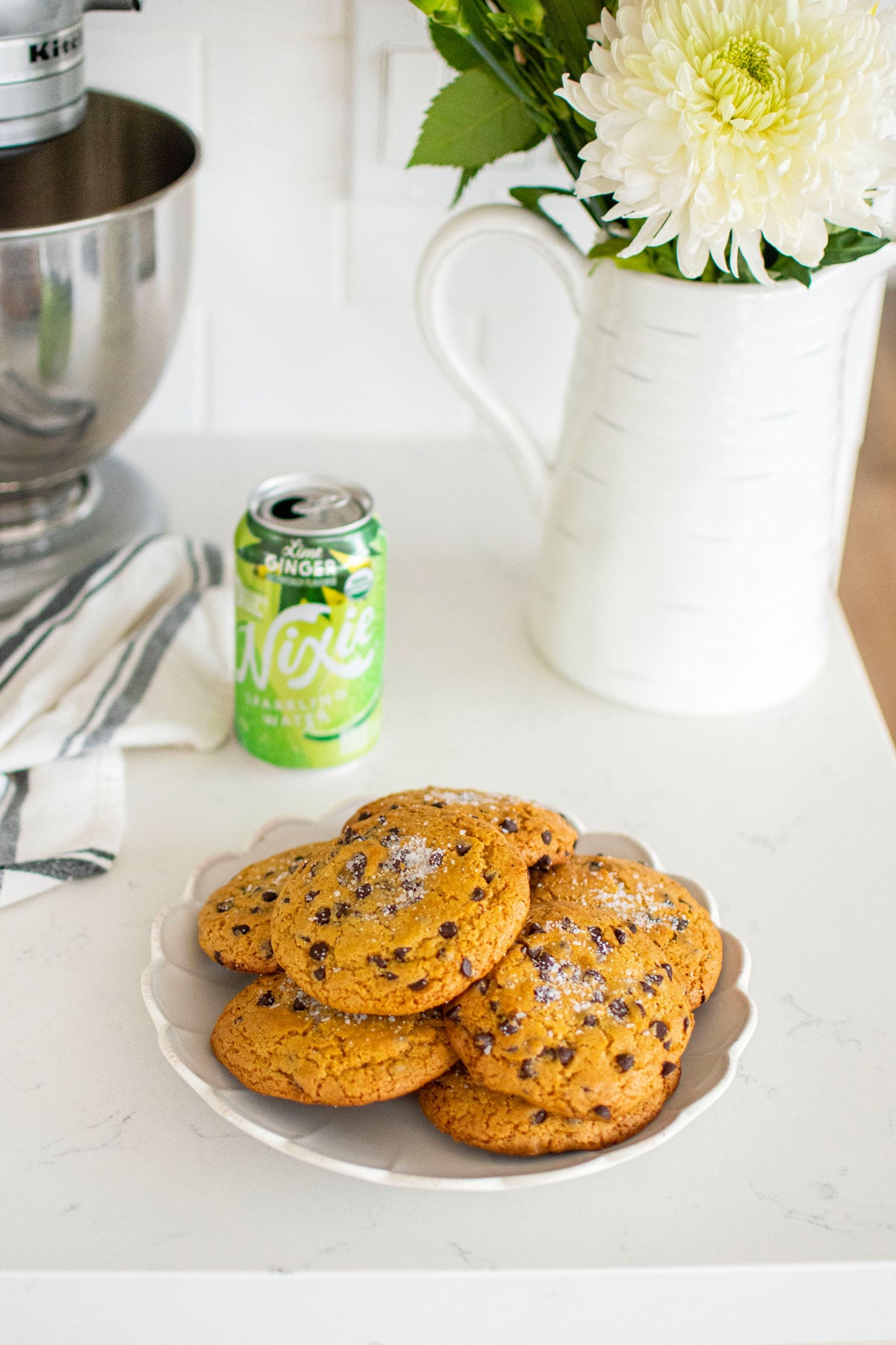 plate of olive oil honey chocolate chip cookies on a white marble counter with fresh flowers and a can of sparkling water.