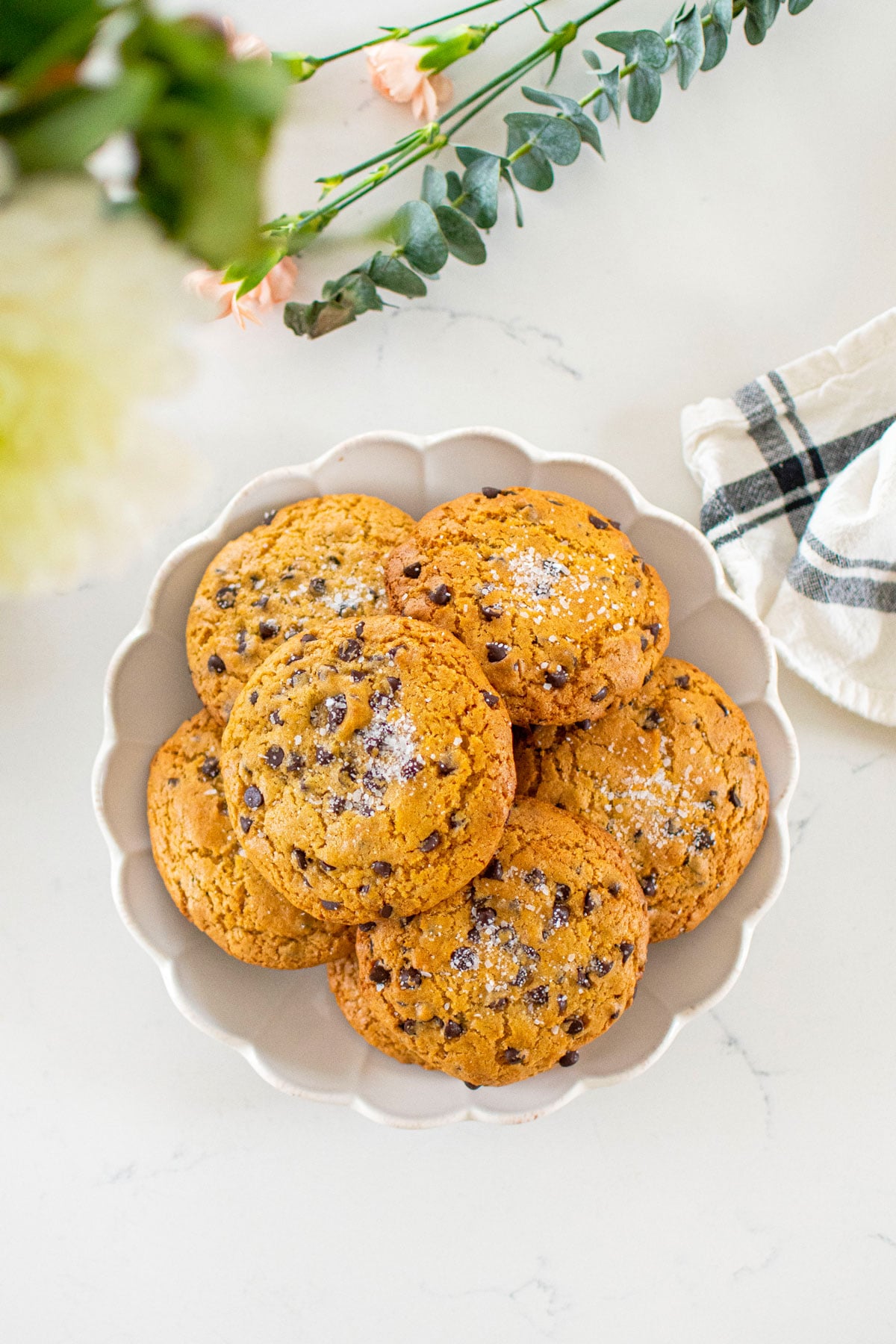 plate of olive oil honey chocolate chip cookies on a white marble counter with fresh flowers.